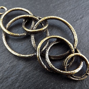 May include: A gold-toned metal pendant with a design of interlocking circles. The pendant has a textured surface and a loop at the top for attaching to a chain.