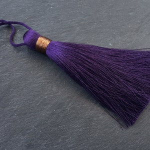 May include: A deep purple tassel with a gold trim. The tassel is made of soft, silky threads and is approximately 5 cm long.
