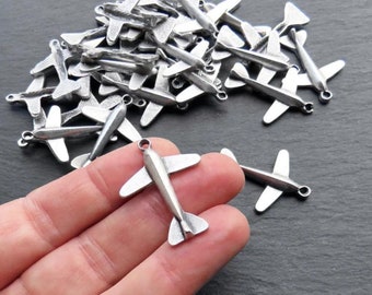 Puede incluir: Un montón de abalorios de avión de plata, algunos están apilados uno encima del otro, y uno está siendo sostenido en una mano. Los abalorios miden aproximadamente 2,5 cm de largo.