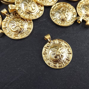 Pode incluir: Um grupo de pingentes de metal dourado com um design de sol e lua. Cada pingente apresenta um design circular com um sol e uma lua no centro, cercados por um anel de s&iacute;mbolos.