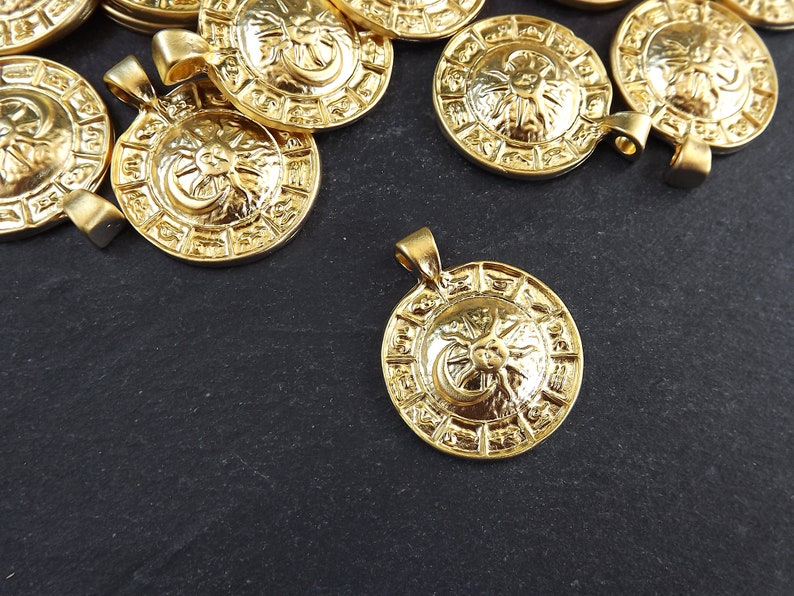 Pode incluir: Um grupo de pingentes de metal dourado com um design de sol e lua. Cada pingente apresenta um design circular com um sol e uma lua no centro, cercados por um anel de s&iacute;mbolos.