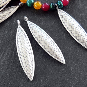 May include: Silver metal leaf-shaped pendant charms with a woven pattern. The charms have a loop at the top for attaching to jewelry.