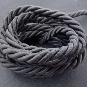 May include: A close-up of a thick, black, braided rope. The rope is coiled into a circle and has a soft, textured surface.