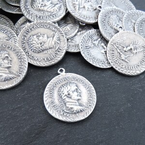 May include: A collection of silver-toned metal charms featuring Roman emperor Antoninus Pius. Each charm has a raised profile of the emperor's head and the inscription "ANTONINVS PIVS AVGGERM" around the edge.
