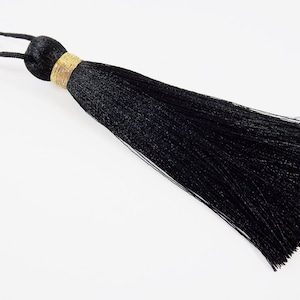 Puede incluir: Un borlón negro con ribete dorado. El borlón está hecho de un material suave y sedoso y tiene una larga franja fluida.