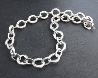 May include: A silver chain necklace with a textured, hammered finish. The chain is made of large, oval-shaped links.