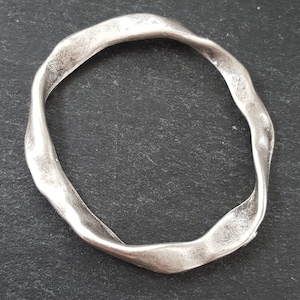 May include: A silver-toned, twisted metal bangle bracelet. The bracelet is smooth and has a slightly textured finish.