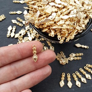 May include: Gold-toned metal pendant charms with a diamond shape and intricate details. The charms have a loop at the top for attaching to jewelry or other crafts.