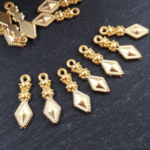 May include: Gold-toned metal pendant charms with a diamond shape and beaded accents. The charms have a loop at the top for attaching to jewelry or other crafts.