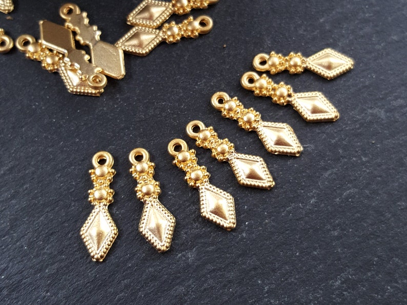 May include: Gold-toned metal pendant charms with a diamond shape and beaded accents. The charms have a loop at the top for attaching to jewelry or other crafts.