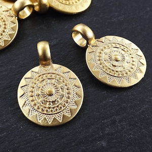 May include: Gold-toned metal pendant charms with a sunburst design. Each charm features a circular center with a smaller sunburst design and a loop for attaching to a chain or cord.