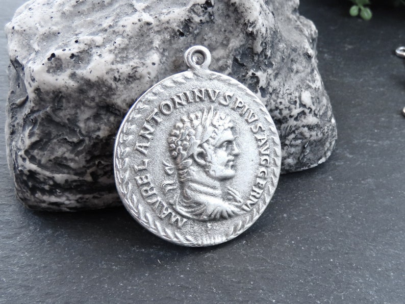 May include: Silver pendant featuring a Roman emperor bust with the inscription "IMP ANTONINVS PIVS AVG" around the edge.