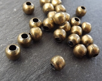 May include: A group of round, antique gold metal beads. The beads have a smooth, slightly textured surface and a hole in the center.