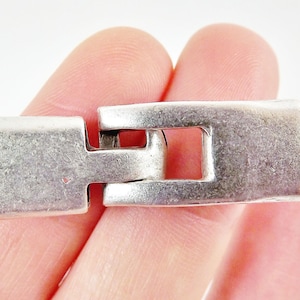 May include: Silver-toned metal clasp with a rectangular shape and a square opening. The clasp is designed to connect two pieces of jewelry or other items.