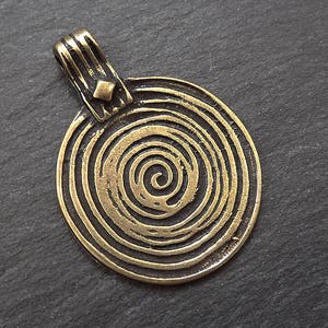 以下が含まれることがあります： 螺旋模様の金色のペンダント。ペンダントはシンプルで幾何学的な形をしており、滑らかで磨かれた仕上げになっています。