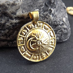 Pode incluir: Pingente dourado com um design circular com s&iacute;mbolos do zod&iacute;aco e um motivo de sol e lua.