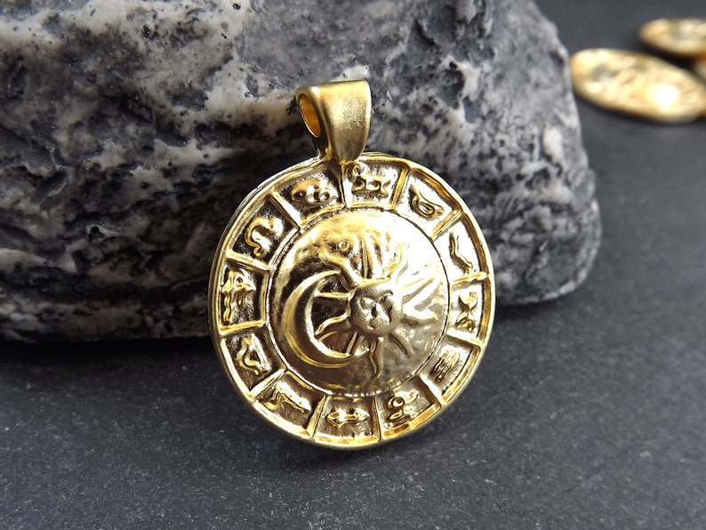 Pode incluir: Pingente dourado com um design circular com s&iacute;mbolos do zod&iacute;aco e um motivo de sol e lua.