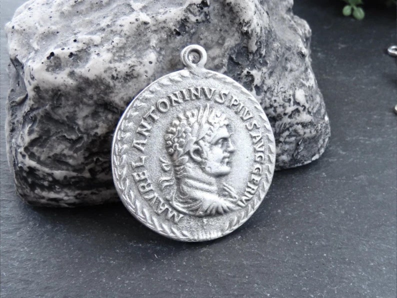 May include: Silver pendant featuring a Roman emperor bust with the inscription "IMP ANTONINVS PIVS AVG" around the edge.