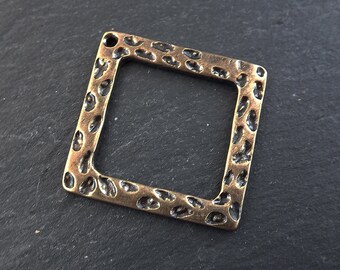 Op de afbeelding: Een vierkant metalen frame met een gehamerde textuur. Het frame heeft een gat aan de bovenkant om op te hangen.