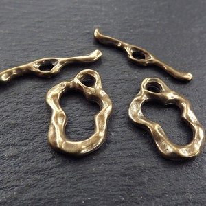 May include: Four antique brass metal jewellery findings. Two are open circles with a textured surface and a hole at the top. Two are long, thin, textured bars with a hole in the centre.