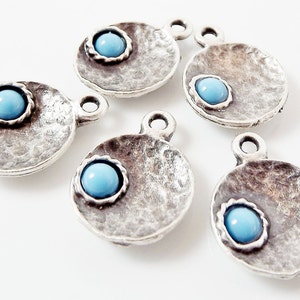 May include: Five silver charm pendants with a light blue gemstone in the center of each. The pendants are round and have a textured surface.