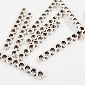 May include: Silver metal chain links in a straight line, forming a decorative piece for jewelry making.