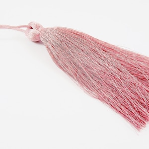 May include: A pink tassel with a long, flowing fringe. The tassel is made of a soft, silky material and has a subtle shimmer.