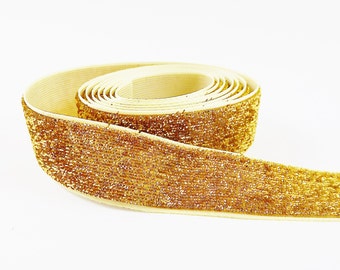 May include: A roll of gold glitter elastic trim with a cream colored backing.