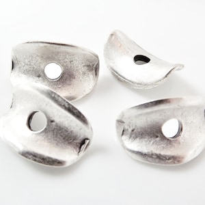 May include: Four silver metal beads with a hole in the centre. The beads are shaped like a half-circle and have a textured surface.