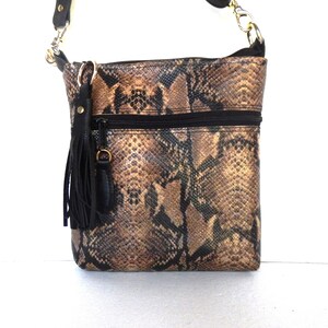 May include: A brown and black snakeskin crossbody bag with a black tassel and a gold chain strap.