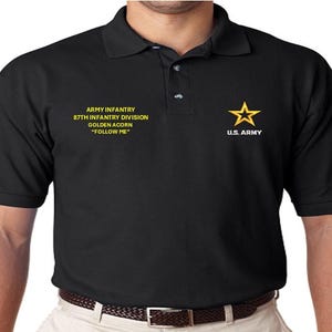 Può includere: Polo nero con testo giallo che recita "Army Infantry 87th Infantry Division Golden Acorn "Follow Me" e una stella gialla con il testo "U.S. Army" sul lato destro della maglietta.