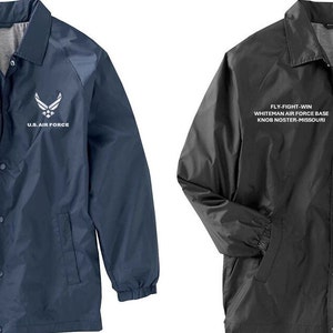 May include: Two baseball jackets with a snap closure. The jacket on the left is navy blue and the jacket on the right is black. Both jackets have the text "FLY-FIGHT-WIN WHITEMAN AIR FORCE BASE KNOS NOSTER MISSOURI" and the U.S. Air Force logo embroidered on the front.