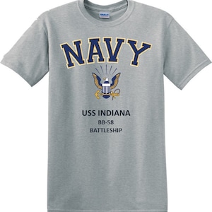 Puede incluir: Una camiseta gris con un texto "NAVY" azul marino y un emblema de águila dorado. El texto "USS INDIANA BB-58 BATTLESHIP" está impreso debajo del emblema.