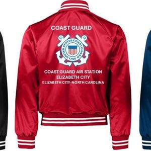 Puede incluir: Tres chaquetas bomber de sat&eacute;n en negro, rojo y azul marino. Cada chaqueta presenta pu&ntilde;os y cuello a rayas blancas, y el texto "COAST GUARD" encima de un emblema de la Guardia Costera y el texto "COAST GUARD AIR STATION ELIZABETH CITY NORTH CAROLINA".