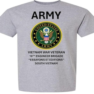 May include: A gray t-shirt with the word "ARMY" in black block letters above a circular emblem. The emblem features an eagle and text that reads "UNITED STATES ARMY". Below the emblem are additional lines of text.