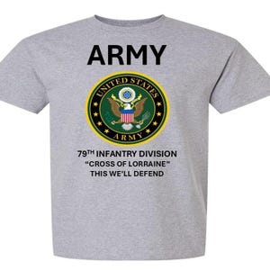 Pode incluir: Uma camiseta cinza com uma estampa preta das palavras "ARMY" e um selo do exército dos Estados Unidos. O selo é verde, dourado e vermelho com uma águia careca e as palavras "UNITED STATES ARMY". Abaixo do selo está o texto "79TH INFANTRY DIVISION "CROSS OF LORRAINE" THIS WE'LL DEFEND"