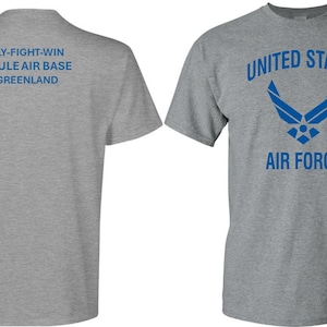 May include: A heather grey t-shirt with a blue graphic of the United States Air Force logo and the text "UNITED STATES AIR FORCE". The back of the shirt has the text "FLY-FIGHT-WIN THULE AIR BASE GREENLAND".