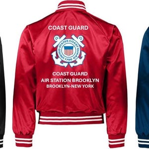 Puede incluir: Tres chaquetas bomber de sat&eacute;n en negro, rojo y azul marino. Cada chaqueta presenta pu&ntilde;os y cuello a rayas blancas, y el texto "COAST GUARD" encima de un emblema de la Guardia Costera y el texto "AIR STATION BROOKLYN BROOKLYN-NEW YORK."