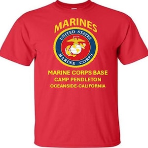 Op de afbeelding: Rood T-shirt met het embleem van de US Marines in een cirkelvormig ontwerp. De tekst bevat "MARINES", "UNITED STATES" en "MARINE CORPS". Daaronder staat "MARINE CORPS BASE CAMP PENDLETON OCEANSIDE-CALIFORNIA".