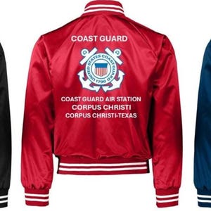 Puede incluir: Tres chaquetas bomber de sat&eacute;n en negro, rojo y azul marino. Cada chaqueta tiene pu&ntilde;os y cuello a rayas blancas y negras. La parte trasera de cada chaqueta muestra las palabras "COAST GUARD" encima de un emblema de la Guardia Costera y el texto "COAST GUARD AIR STATION CORPUS CHRISTI-TEXAS."