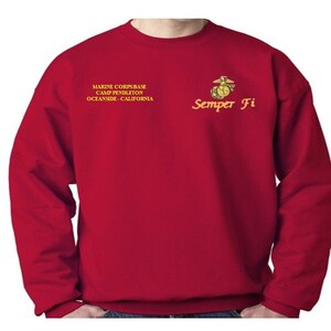 May include: Red sweatshirt with a gold embroidered Marine Corps emblem and the text "Semper Fi" on the right side of the chest. The text "Marine Corps Base Camp Pendleton Oceanside, California" is embroidered on the left side of the chest.