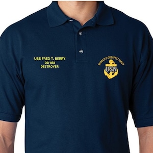 Puede incluir: Una camiseta polo azul marino con el texto "USS FRED T. BERRY DD-858 DESTROYER" y un ancla bordada en oro con el texto "WORLD'S GREATEST NAVY USN" en el pecho derecho.