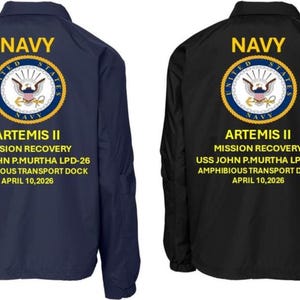 Op de afbeelding: Twee marineblauwe en zwarte jassen met het woord "NAVY" in gouden letters boven een cirkelvormig embleem. Onder het embleem staat de tekst "ARTEMIS II MISSION RECOVERY USS JOHN P.MURTHA LPD-26 AMPHIBIOUS TRANSPORT DOCK APRIL 10,2026".