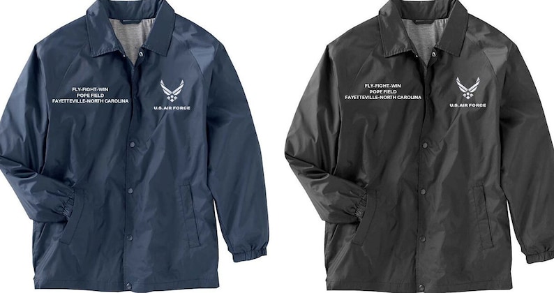 May include: Two lightweight jackets with snap closures. The jacket on the left is navy blue with white text and a U.S. Air Force logo. The jacket on the right is black with white text and a U.S. Air Force logo. Both jackets have "FLY-FIGHT-WIN POPE FIELD FAYETTEVILLE-NORTH CAROLINA" text on the front.