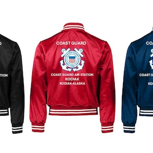 May include: Three satin bomber jackets in black, red, and navy blue. Each jacket has white and black striped trim on the collar, cuffs, and hem. The back of each jacket displays the words "COAST GUARD" above a Coast Guard emblem and text that reads "COAST GUARD AIR STATION KODIAK KODIAK-ALASKA."