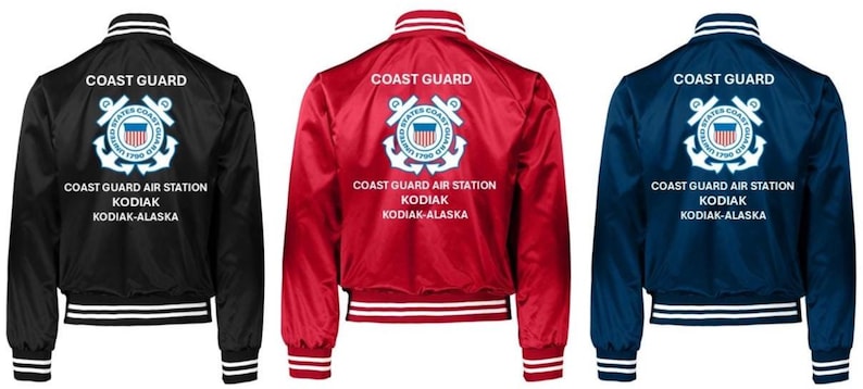 Puede incluir: Tres chaquetas bomber de sat&eacute;n en negro, rojo y azul marino. Cada chaqueta tiene pu&ntilde;os, cuello y dobladillo a rayas blancas y azules. La parte trasera de cada chaqueta muestra las palabras "COAST GUARD" encima de un emblema de la Guardia Costera y el texto "COAST GUARD AIR STATION KODIAK-ALASKA."