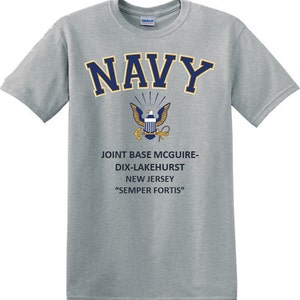 May include: A grey t-shirt with a navy blue "NAVY" graphic, a gold eagle emblem, and the text "JOINT BASE MCGUIRE-DIX-LAKEHURST NEW JERSEY "SEMPER FORTIS""