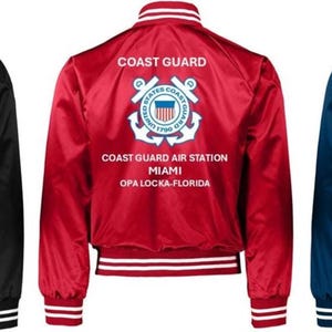 Puede incluir: Tres chaquetas bomber de la Guardia Costera de sat&eacute;n en negro, rojo y azul marino. Cada chaqueta tiene pu&ntilde;os, cuello y dobladillo a rayas blancas. El emblema de la Guardia Costera y el texto "COAST GUARD AIR STATION MIAMI OPA LOCKA-FLORIDA" est&aacute;n impresos en la espalda.