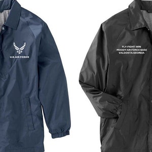 May include: Two lightweight jackets with snap closures. The jacket on the left is navy blue with white text and a white Air Force logo. The jacket on the right is black with white text and a white Air Force logo. Both jackets say "FLY-FIGHT-WIN", "MOODY AIR FORCE BASE", "VALDOSTA-GEORGIA", and "U.S. AIR FORCE".