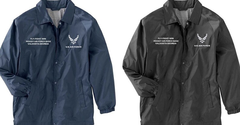 May include: Two lightweight jackets with snap closures. The jacket on the left is navy blue with white text and a white Air Force logo. The jacket on the right is black with white text and a white Air Force logo. Both jackets say "FLY-FIGHT-WIN", "MOODY AIR FORCE BASE", "VALDOSTA-GEORGIA", and "U.S. AIR FORCE".